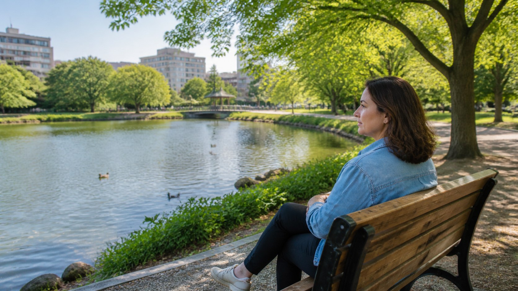 Adult sitting beside an urban park lake during a nature and mental well-being break
